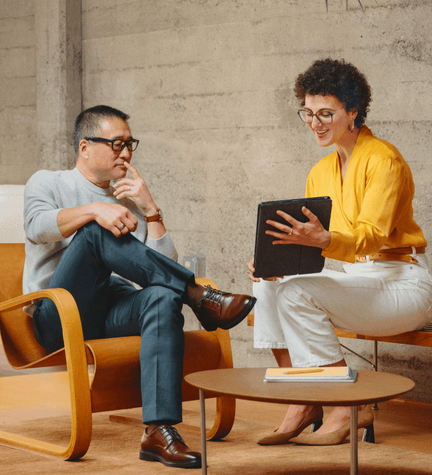 Two office workers in warmly lit seating area looking at a tablet
